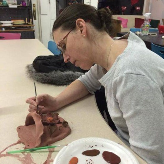 Woman painting a hand sculpted red clay wall vase