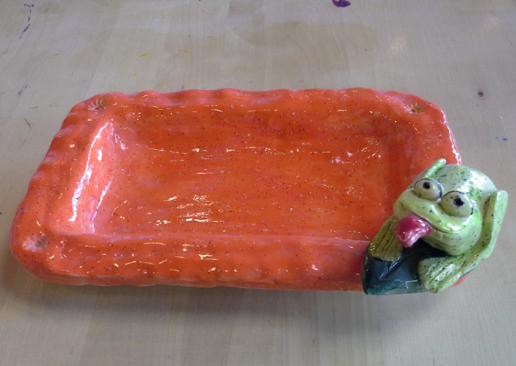 Orange rectangular clay dish with green frog sclupture on the corner sticking out it's tongue